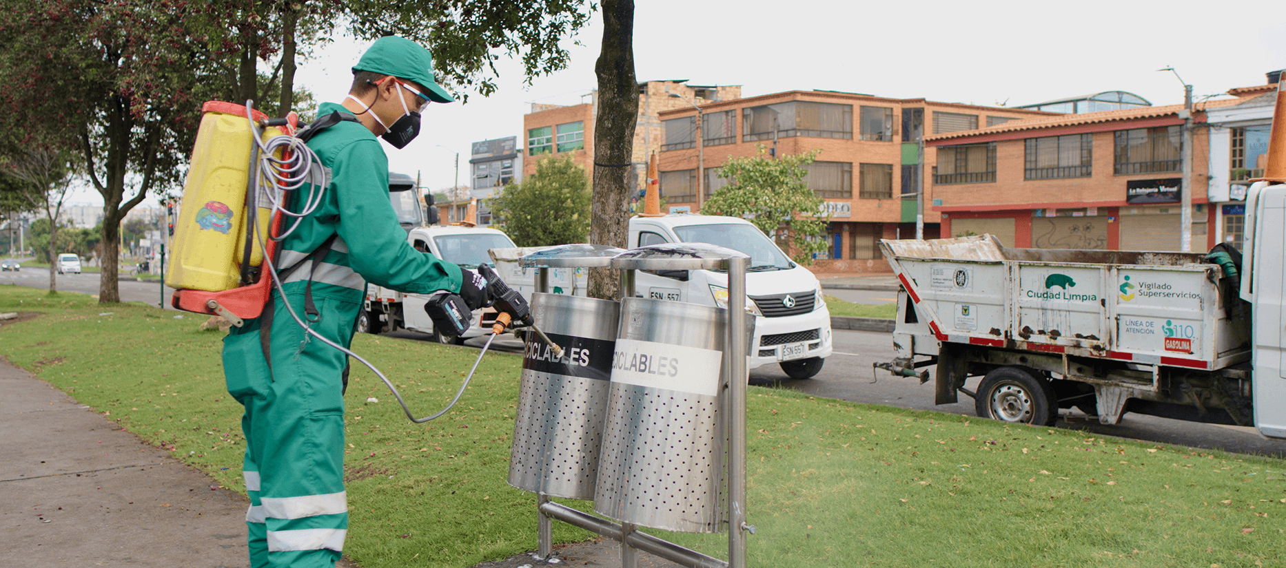 Colaborador de Ciudad Limpia realizando labores de desinfección y mantenimiento en una zona verde urbana, aplicando producto sobre puntos de disposición para residuos.