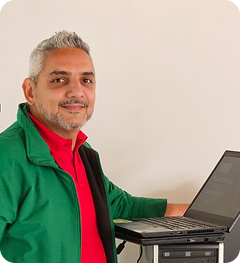 Colaborador de Ciudad Limpia posa junto a un computador portátil en un espacio interior, con expresión amable y actitud profesional.