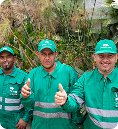 Tres colaboradores de Ciudad Limpia posando frente a una zona verde y haciendo gesto de aprobación con el pulgar, durante una jornada de trabajo.