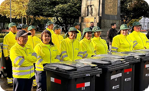 Grupo de colaboradores de Ciudad Limpia, con uniformes reflectivos amarillos, participando en una jornada operativa junto a varios contenedores de residuos en un espacio público.