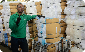 Colaborador de Ciudad Limpia posa en una zona de almacenamiento de excedentes industriales, rodeado de pacas compactadas de plástico y cartón listas para su gestión y clasificación.